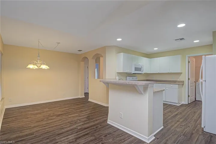 Kitchen with white appliances, white cabinets, a kitchen breakfast bar, dark hardwood / wood-style floors, and kitchen peninsula