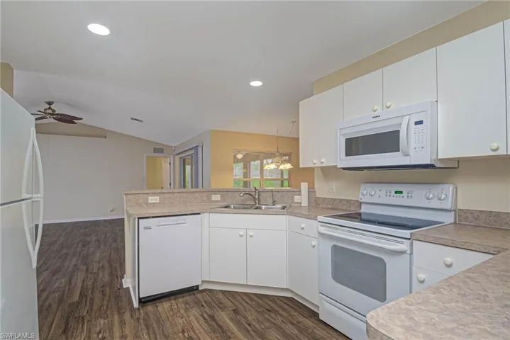 Kitchen with white appliances, white cabinets, decorative light fixtures, sink, and kitchen peninsula