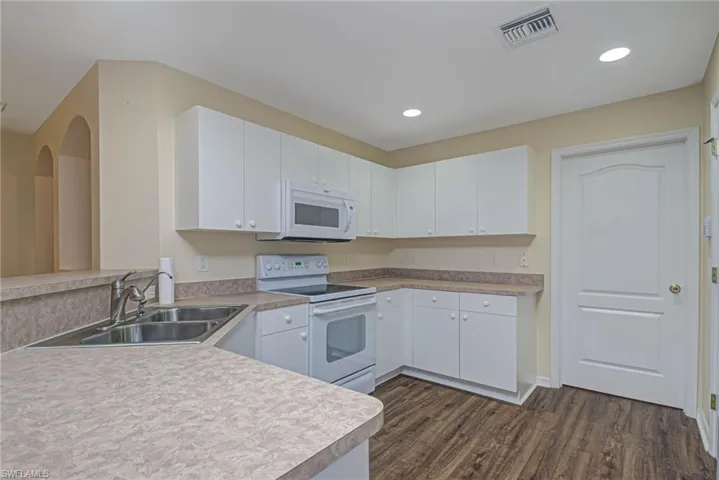 Kitchen with white cabinetry, kitchen peninsula, white appliances, dark wood-type flooring, and sink