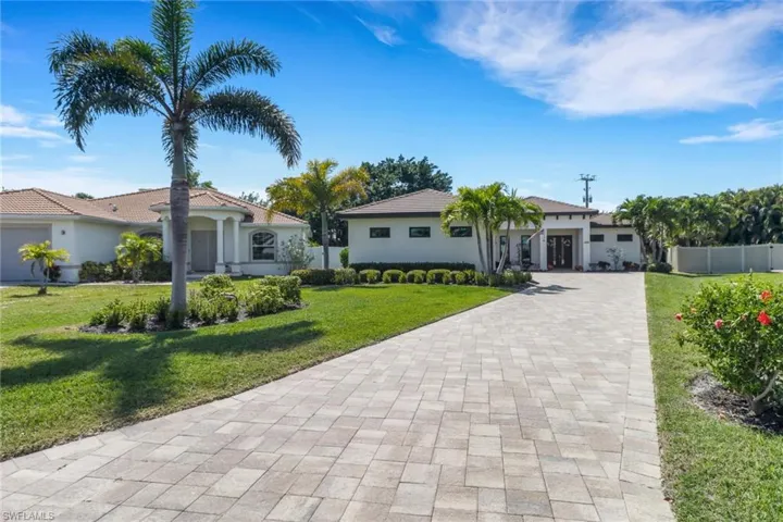 View of front of house featuring a front yard, decorative driveway, stucco siding, and fence