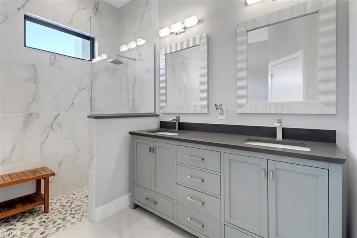 Bathroom with a marble finish shower, double vanity, a sink, and marble finish floor