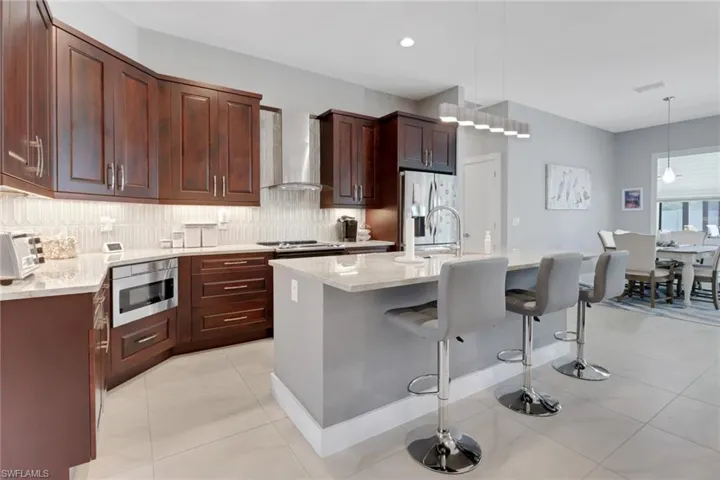 Kitchen with decorative backsplash, stainless steel fridge, wall chimney exhaust hood, built in microwave, and pendant lighting
