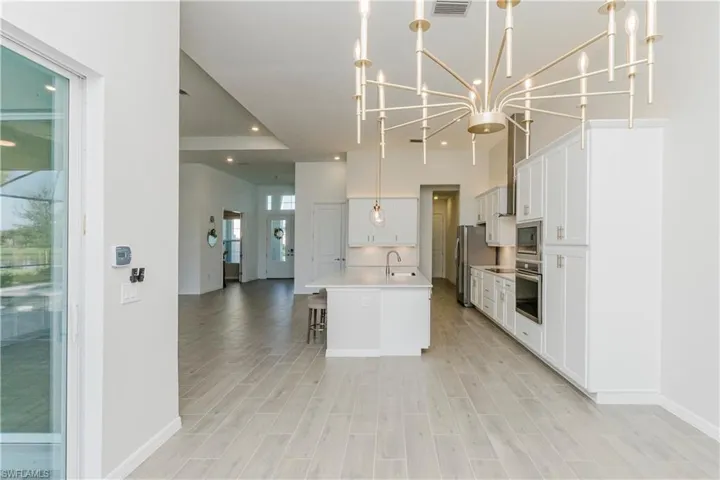 Kitchen with a chandelier, a kitchen bar, an island with sink, open floor plan, and white cabinetry