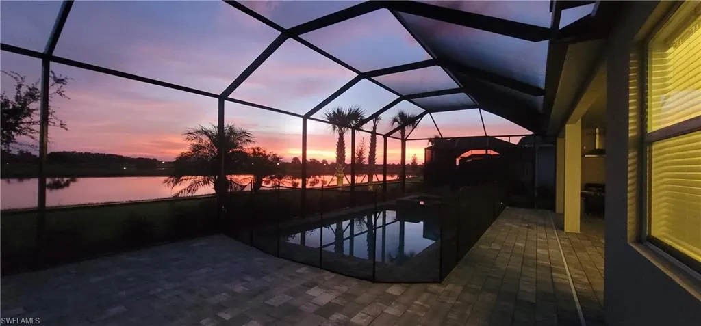 Pool at dusk featuring screened in enclosure, a sunroom, an outdoor pool, and a water view