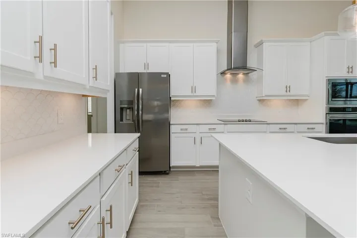 Kitchen with tasteful backsplash, stainless steel appliances, wall chimney exhaust hood, and white cabinetry