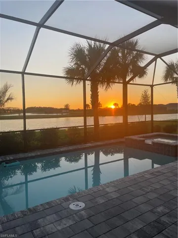 Pool at dusk featuring a sunroom, glass enclosure, a pool with connected hot tub, and a water view