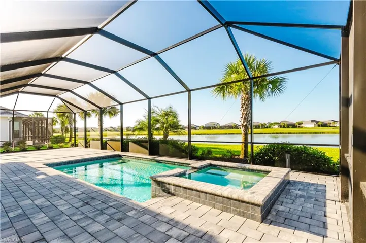 View of pool featuring a sunroom, glass enclosure, a pool with connected hot tub, a water view, and a patio area