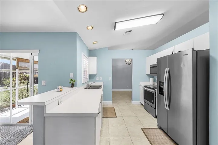 Kitchen with stainless steel appliances, light countertops, a peninsula, white cabinetry, and recessed lighting