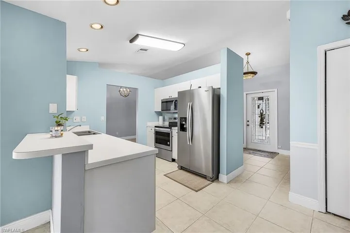 Kitchen with stainless steel appliances, light countertops, white cabinetry, a kitchen bar, and a peninsula