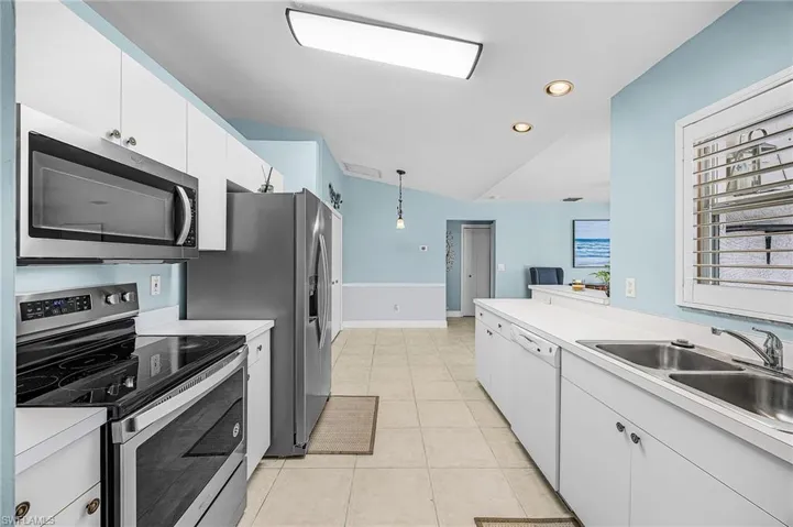 Kitchen with stainless steel appliances, light countertops, white cabinetry, decorative light fixtures, and light tile patterned flooring
