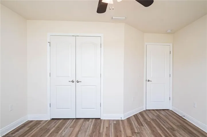 Unfurnished bedroom with ceiling fan, wood finished floors, visible vents, baseboards, and a closet
