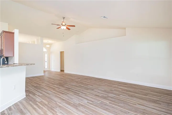 Unfurnished living room featuring light wood finished floors, visible vents, baseboards, ceiling fan, and vaulted ceiling