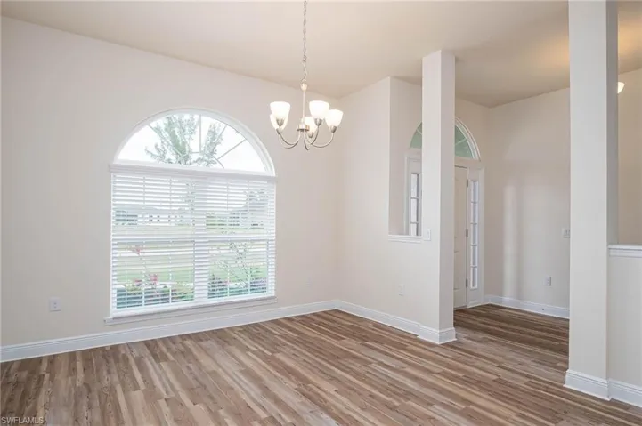 Empty room featuring a notable chandelier, wood finished floors, and baseboards
