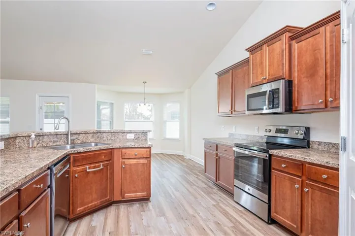 Kitchen featuring lofted ceiling, stainless steel appliances, a sink, light wood finished floors, and brown cabinetry