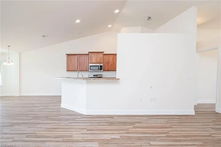 Kitchen with light wood-type flooring, visible vents, stainless steel microwave, and brown cabinets