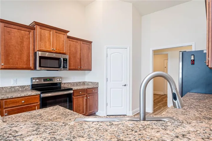 Kitchen with stainless steel appliances, brown cabinetry, a sink, and high vaulted ceiling