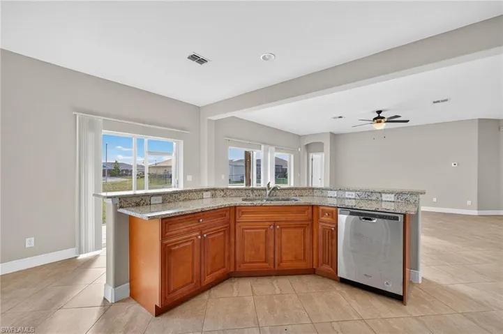 Kitchen featuring an island with sink, brown cabinetry, stainless steel dishwasher, and plenty of natural light
