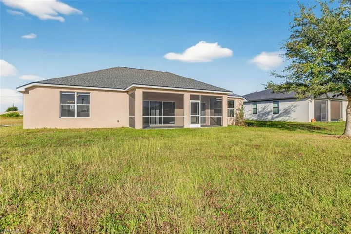 Back of property with a yard, a sunroom, stucco siding, and roof with shingles