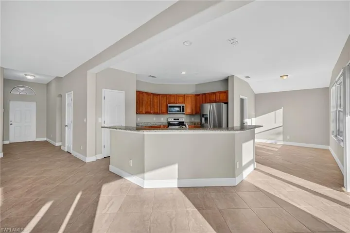 Kitchen with stainless steel appliances, brown cabinetry, recessed lighting, dark stone countertops, and light tile patterned floors