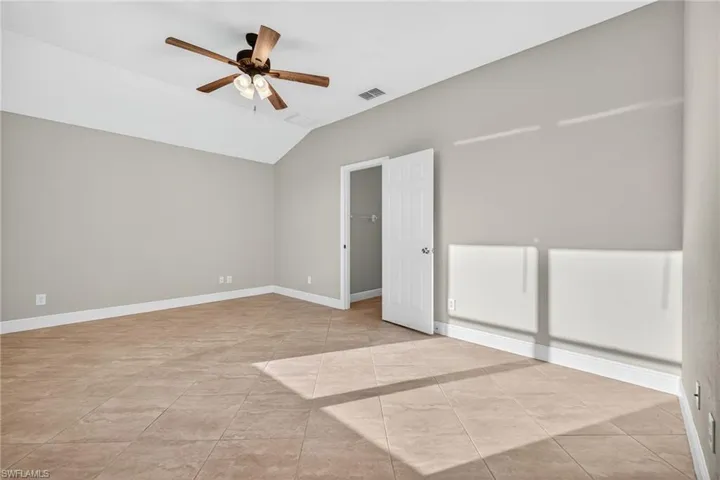 Empty room with lofted ceiling, ceiling fan, and light tile patterned floors