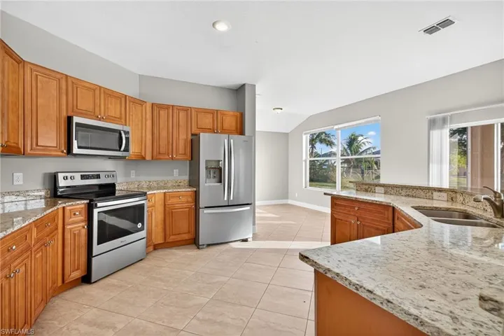Kitchen with stainless steel appliances, light tile patterned floors, light stone countertops, brown cabinets, and lofted ceiling
