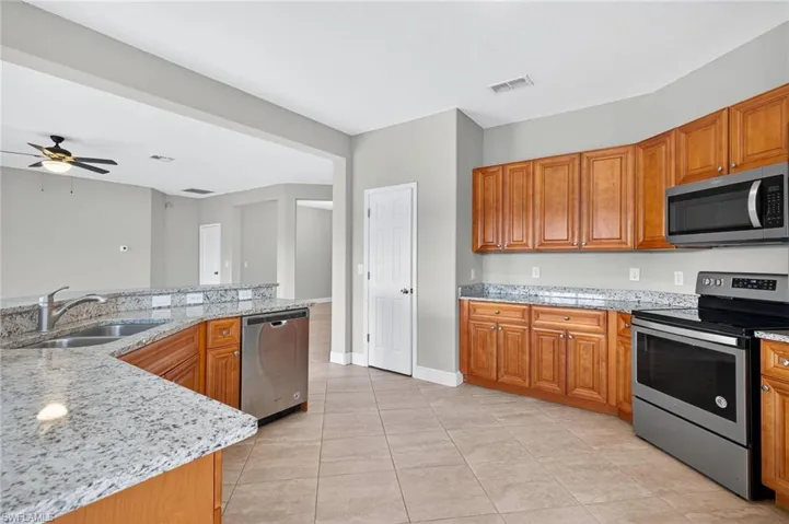 Kitchen featuring stainless steel appliances, light stone counters, light tile patterned floors, brown cabinets, and a ceiling fan