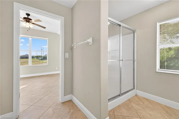 Full bathroom featuring light tile patterned flooring, ceiling fan, a stall shower, and healthy amount of natural light