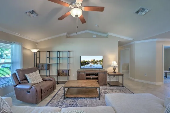 Living room featuring ceiling fan, light tile patterned flooring, lofted ceiling, and ornamental molding