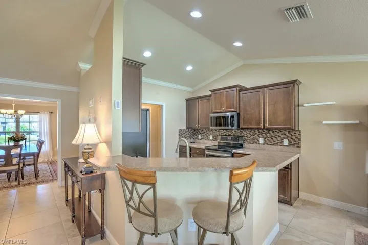 Kitchen featuring crown molding, decorative backsplash, appliances with stainless steel finishes, a breakfast bar area, and kitchen peninsula