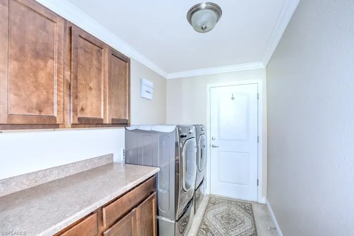 Laundry area featuring cabinets, washing machine and clothes dryer, and crown molding