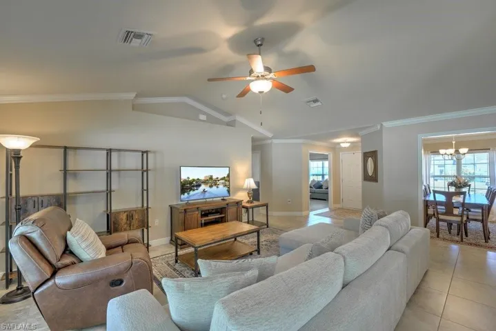 Living room featuring ornamental molding, light tile patterned floors, vaulted ceiling, and a healthy amount of sunlight