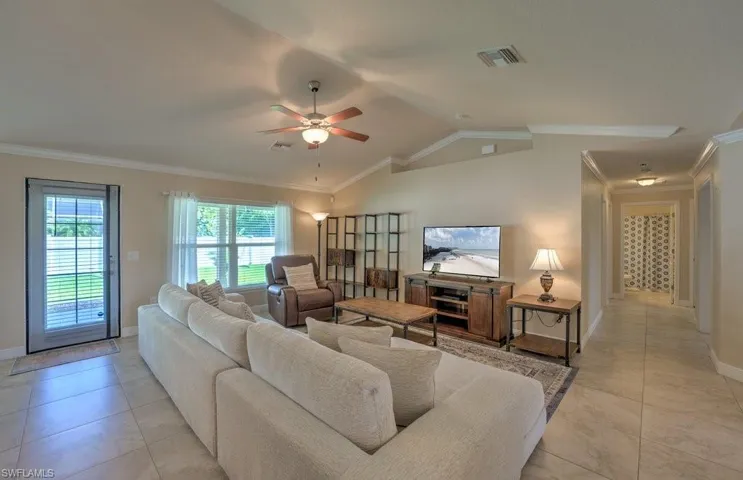 Living room with lofted ceiling, crown molding, light tile patterned floors, and ceiling fan