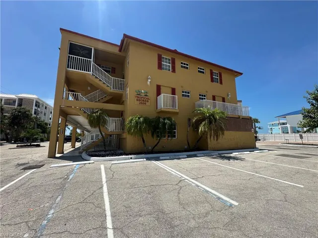 Multi-story building featuring exterior walkways and balconies, red window shutters, and designated parking spaces