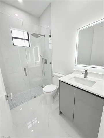 Full bath with toilet, vanity, marble tiled flooring, and a marble finish shower
