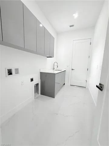 Laundry area featuring hookup for an electric dryer, cabinet space, light marble finish floors, baseboards, and hookup for a washing machine