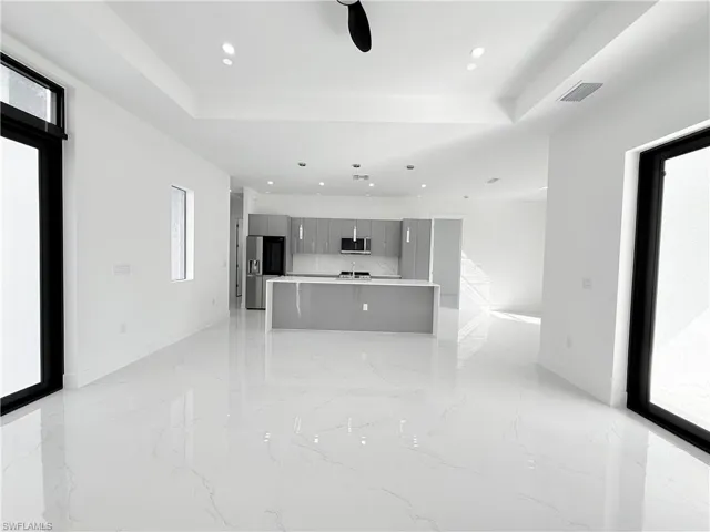 Unfurnished living room with healthy amount of natural light, light marble finish flooring, a tray ceiling, and recessed lighting