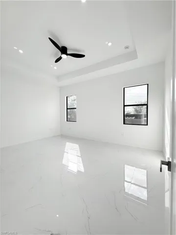 Empty room featuring a raised ceiling, light marble finish floors, baseboards, and recessed lighting