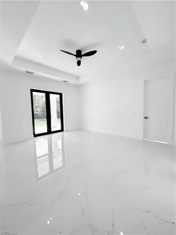 Empty room featuring a raised ceiling, light marble finish floors, a ceiling fan, recessed lighting, and baseboards
