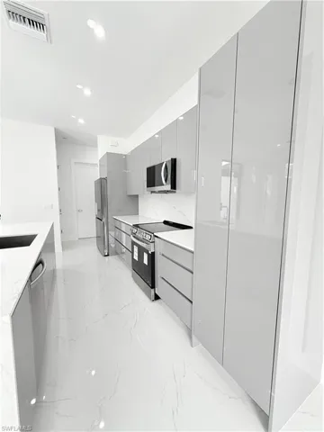 Kitchen featuring modern cabinets, range, gray cabinetry, light marble finish floors, and refrigerator