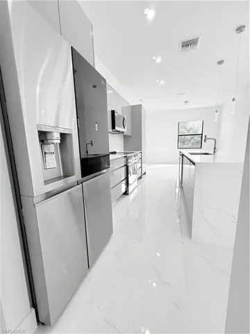 Kitchen featuring modern cabinets, electric stove, refrigerator, a sink, and light marble finish floors
