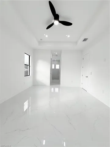 Empty room featuring a raised ceiling, light marble finish floors, a ceiling fan, and recessed lighting