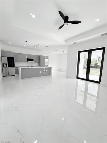 Unfurnished living room featuring a raised ceiling, light marble finish flooring, a ceiling fan, recessed lighting, and french doors
