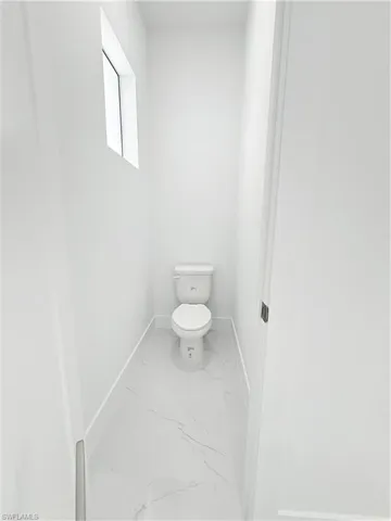 Bathroom with marble look tiles, baseboards, and toilet