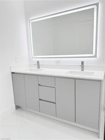 Bathroom with double vanity, marble finish flooring, and baseboards