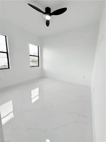 Unfurnished room with light marble finish floors, baseboards, and a ceiling fan