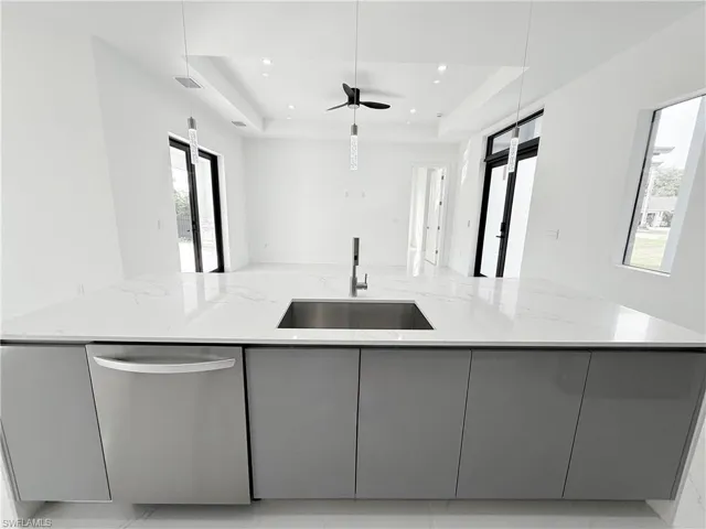 Kitchen featuring stainless steel dishwasher, gray cabinets, a sink, a tray ceiling, and light stone counters