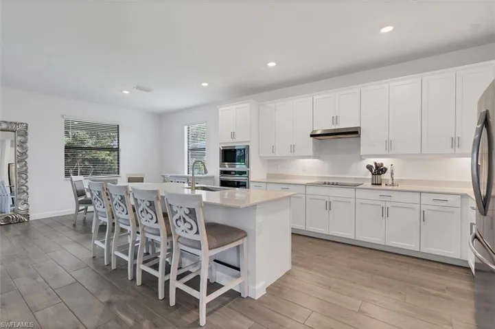 Kitchen featuring white cabinetry, a center island with sink, recessed lighting, a breakfast bar, and light wood-style flooring