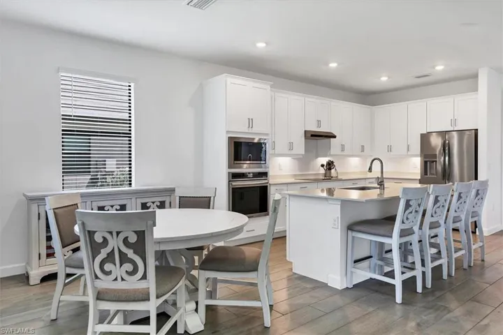 Kitchen featuring white cabinetry, stainless steel appliances, a breakfast bar area, light wood-type flooring, and a kitchen island with sink