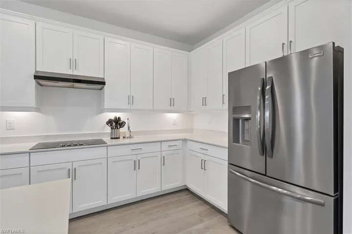 Kitchen with stainless steel fridge, white cabinets, under cabinet range hood, light wood-style floors, and black electric stovetop
