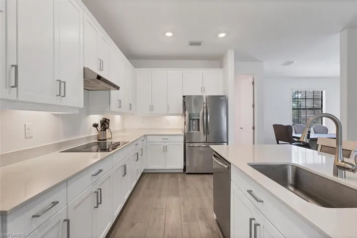 Kitchen featuring appliances with stainless steel finishes, white cabinetry, light wood-style floors, under cabinet range hood, and recessed lighting